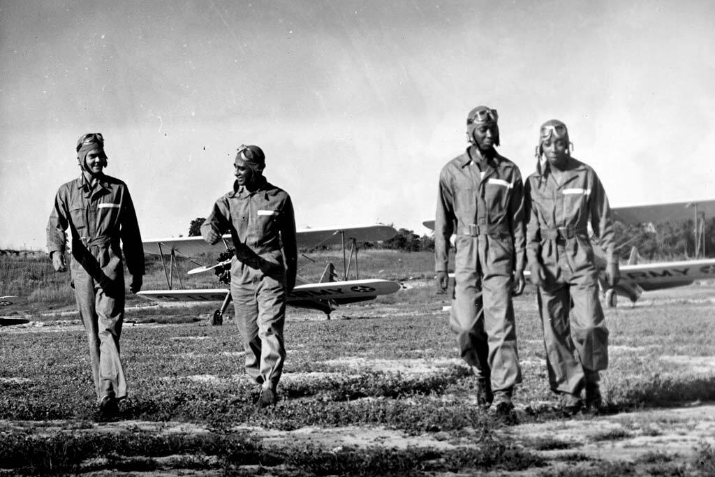 Four men walking away from airplanes in the background.