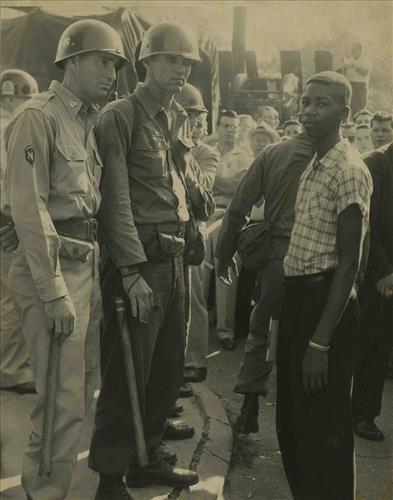 Two white Arkansas National Guardsmen stand in front of a young Black man.