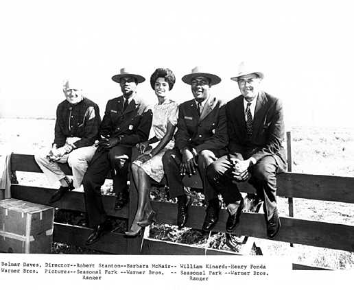 Five people stiting on a fence, two in National Park Service uniforms, three in civilian clothing.